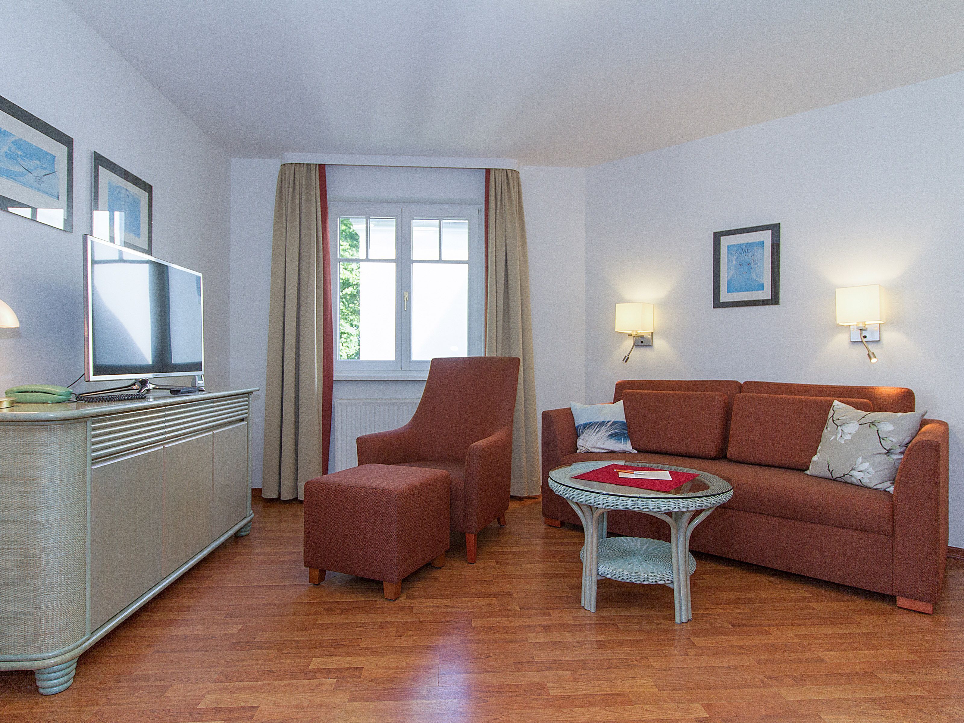 A hotel room with a sofa, armchair, small table, and a desk with a computer.