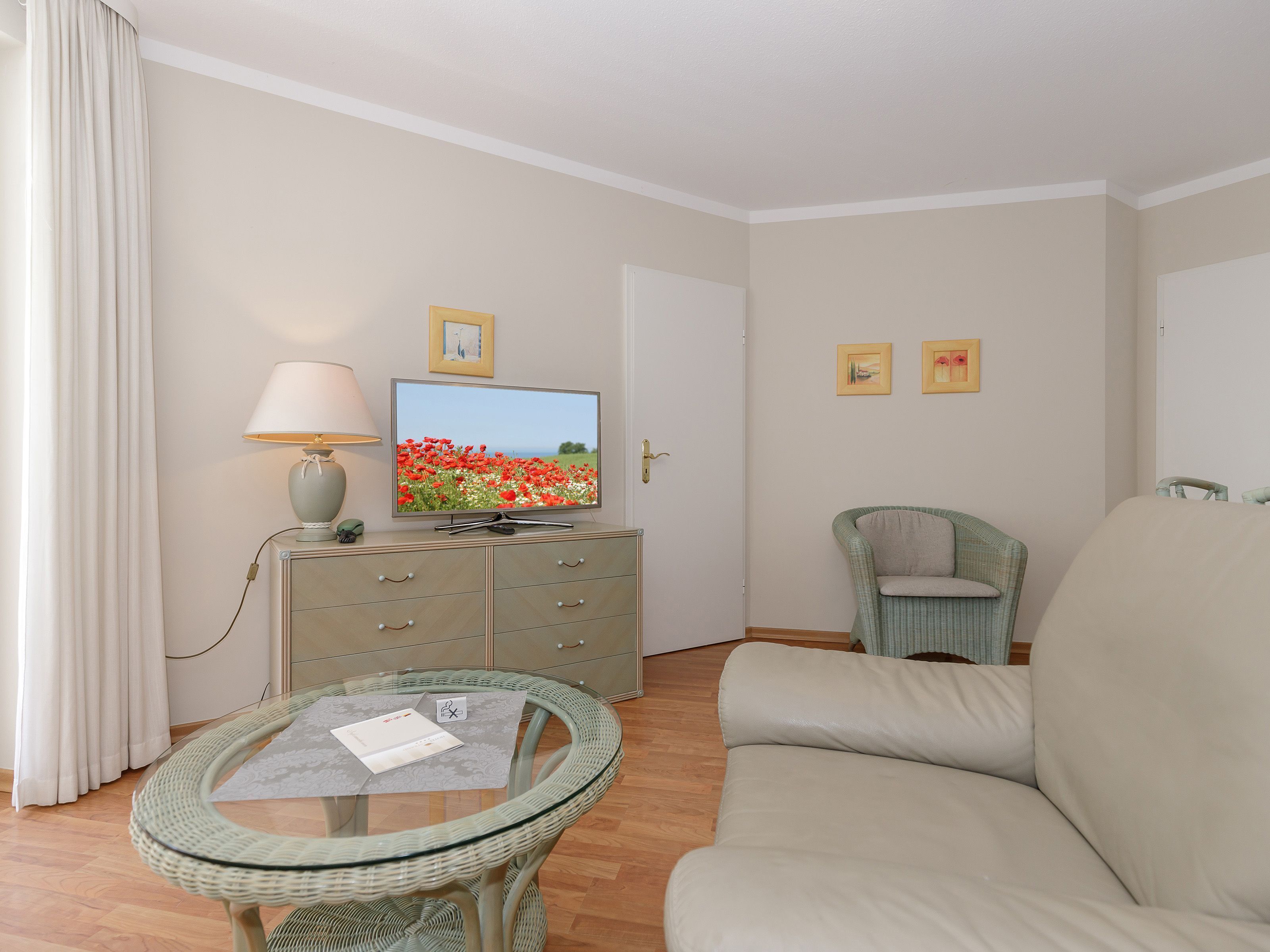 A room with a television, a glass table, a sofa, a chair, and a dresser.