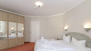 Una habitación de hotel con cama, armario, espejo e iluminación en la pared.