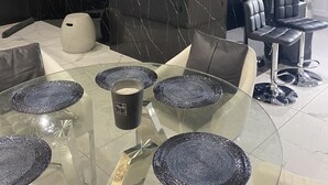 Een moderne eetruimte met een glazen tafel, zwarte marmeren wanden en zwarte lederen stoelen.