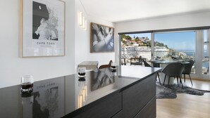 A modern kitchen with a large island, framed artwork, and a view of the coastline. - Seacliffe 502 (Cape Town)