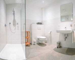 Un baño moderno con cabina de ducha de vidrio, inodoro, lavabo y un pequeño estante de madera.