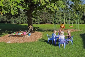 Un grupo de niños jugando debajo de un árbol con un columpio en un parque.