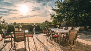 Un patio exterior con mesa y sillas, rodeado de follaje y un cielo despejado.