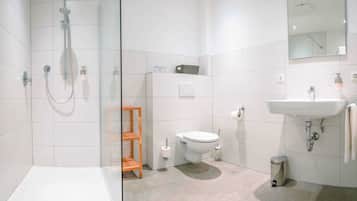 A modern bathroom with a glass shower enclosure, a toilet, a sink, and a small wooden shelf.