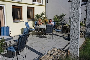 Un patio al aire libre con sillas y mesas, un muro de piedra y un edificio con ventanas.