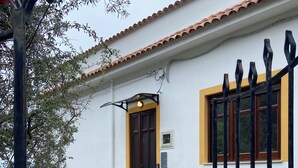 Un chemin menant à un bâtiment doté d’une porte marron, d’une fenêtre avec un cadre jaune et d’une clôture en métal noir.