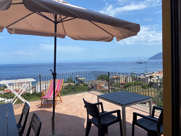 Een terras met een tafel en stoelen, een gestreepte strandstoel en een grote parasol.