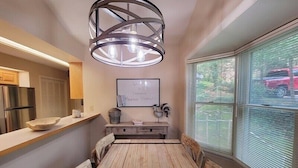 A kitchen with a wooden table, a modern pendant light, and a view of the street through large windows. - Fairway Mountain Retreat-Views-5min to Downtown (Waynesville)