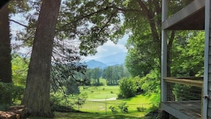 A view from a covered outdoor area with a wooden deck, a grassy lawn, and a golf course in the distance. - Fairway Mountain Retreat-Views-5min to Downtown (Waynesville)