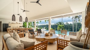 A spacious living area with a round wooden coffee table, comfortable seating, and a view of a lush tropical landscape. - Amazing Jungle View Villa, 4 BR, Ubud With Staff (Ubud)