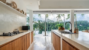 A modern kitchen with wooden cabinets, a large island, and a view of lush greenery. - Amazing Jungle View Villa, 4 BR, Ubud With Staff (Ubud)
