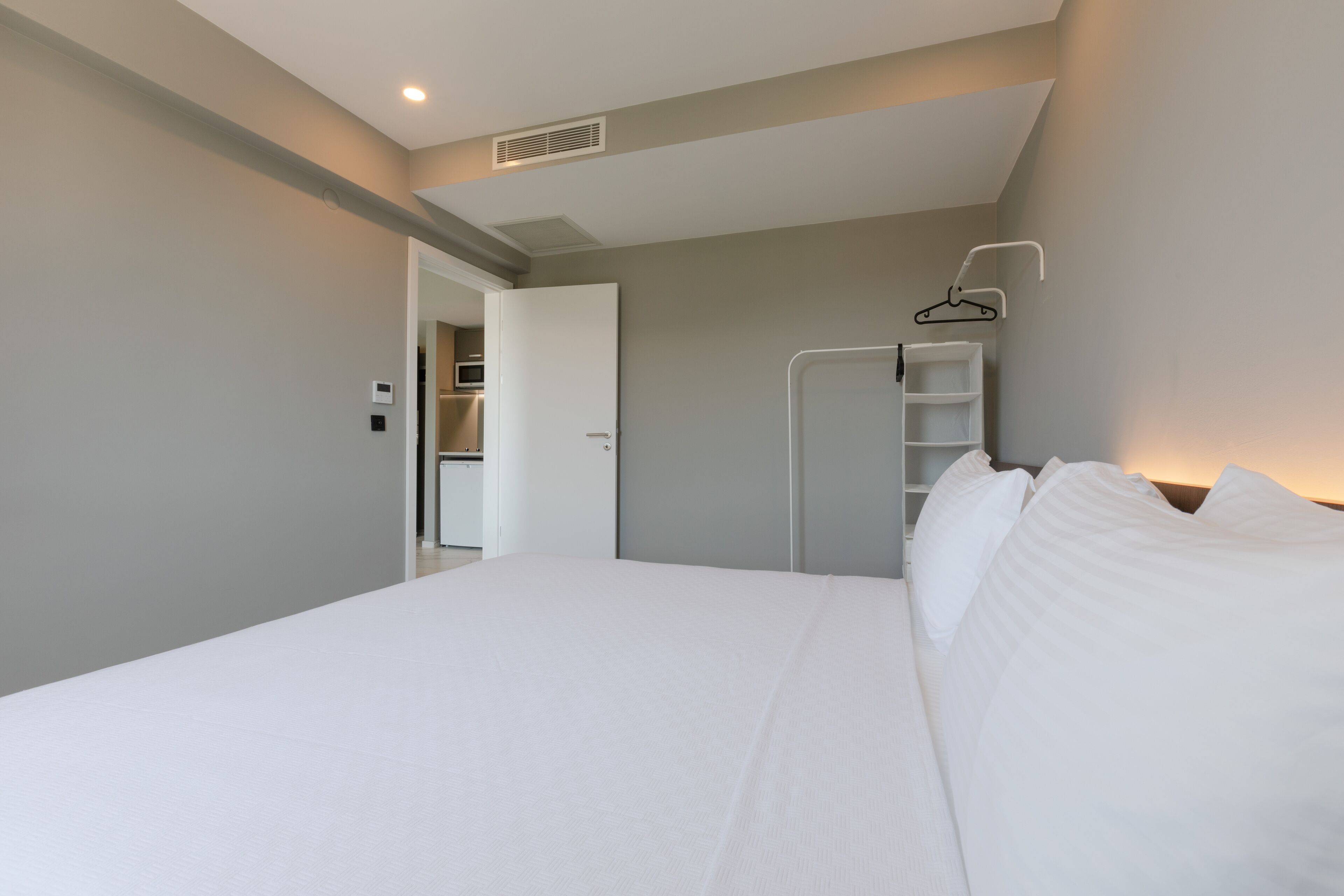 Una habitación de hotel moderna con una cama bien hecha, un vestidor y una percha para ropa.