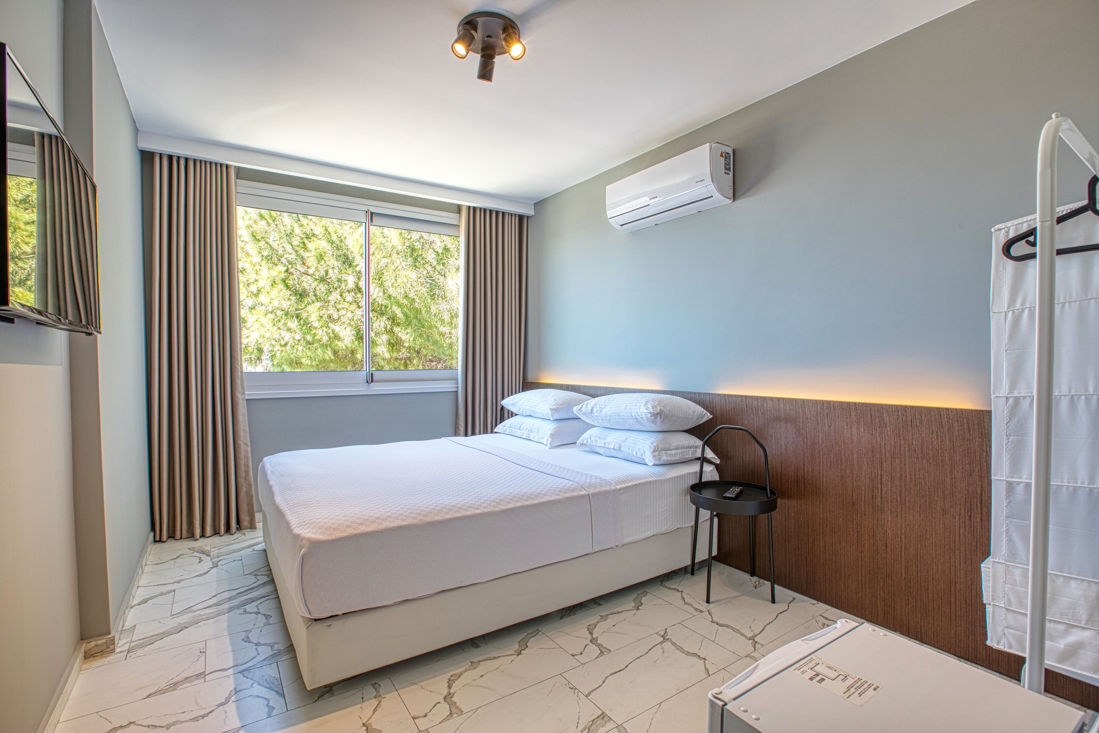 A modern bedroom with a large bed, an air conditioning unit, a small table, and a window with curtains.
