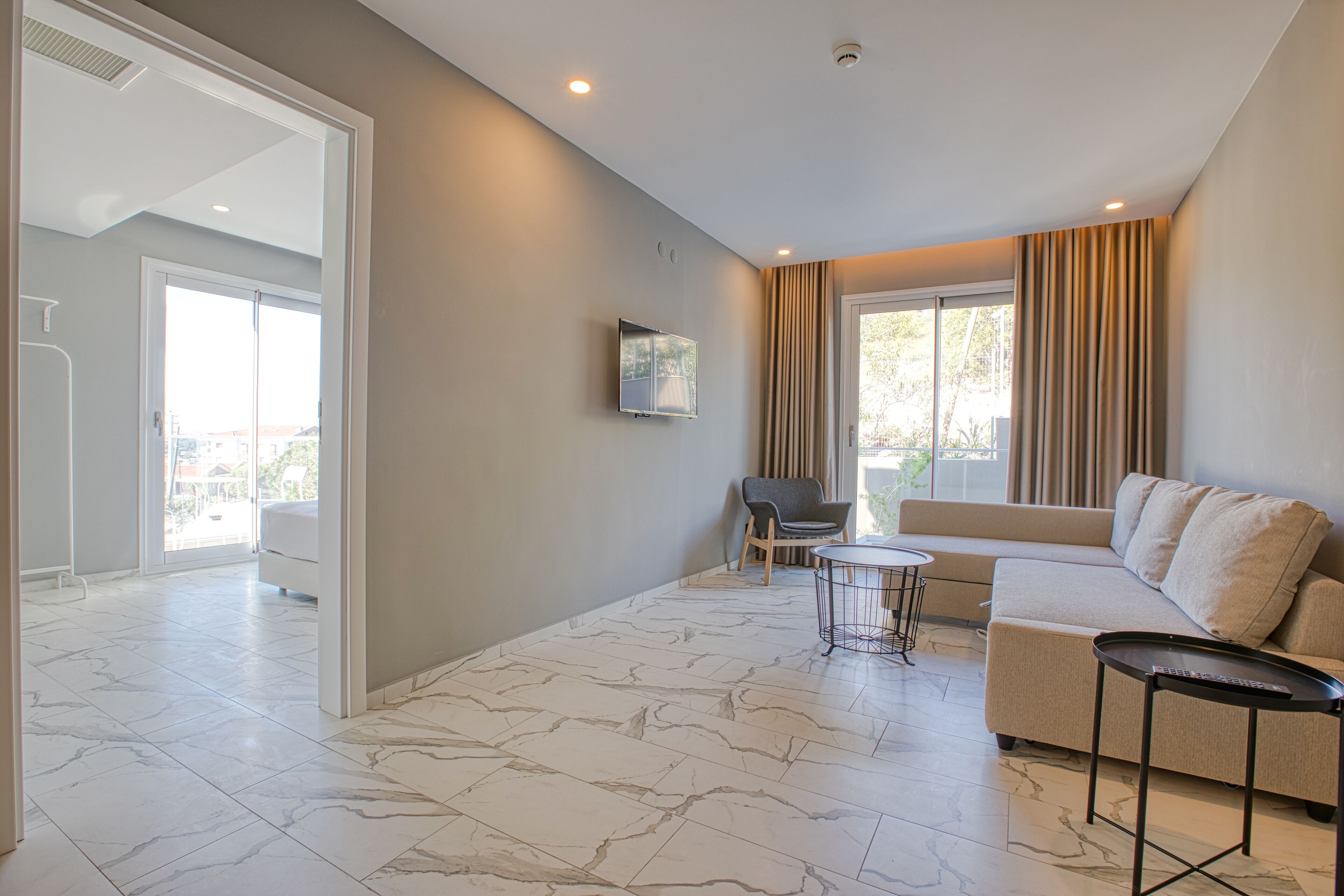 A modern living room with a marble floor, a beige sofa, a small round table, and a TV mounted on the wall.