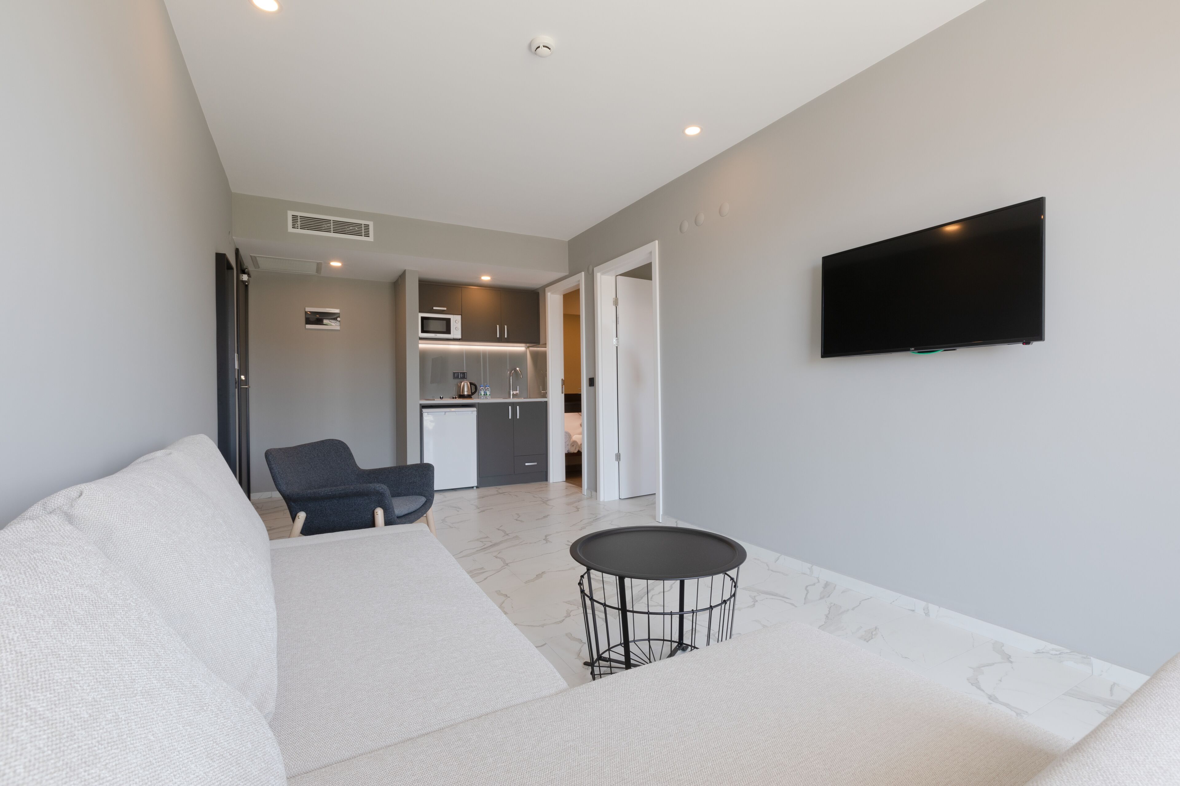Een moderne woonkamer met een bank, een klein rond tafeltje en een flatscreen televisie aan de muur.