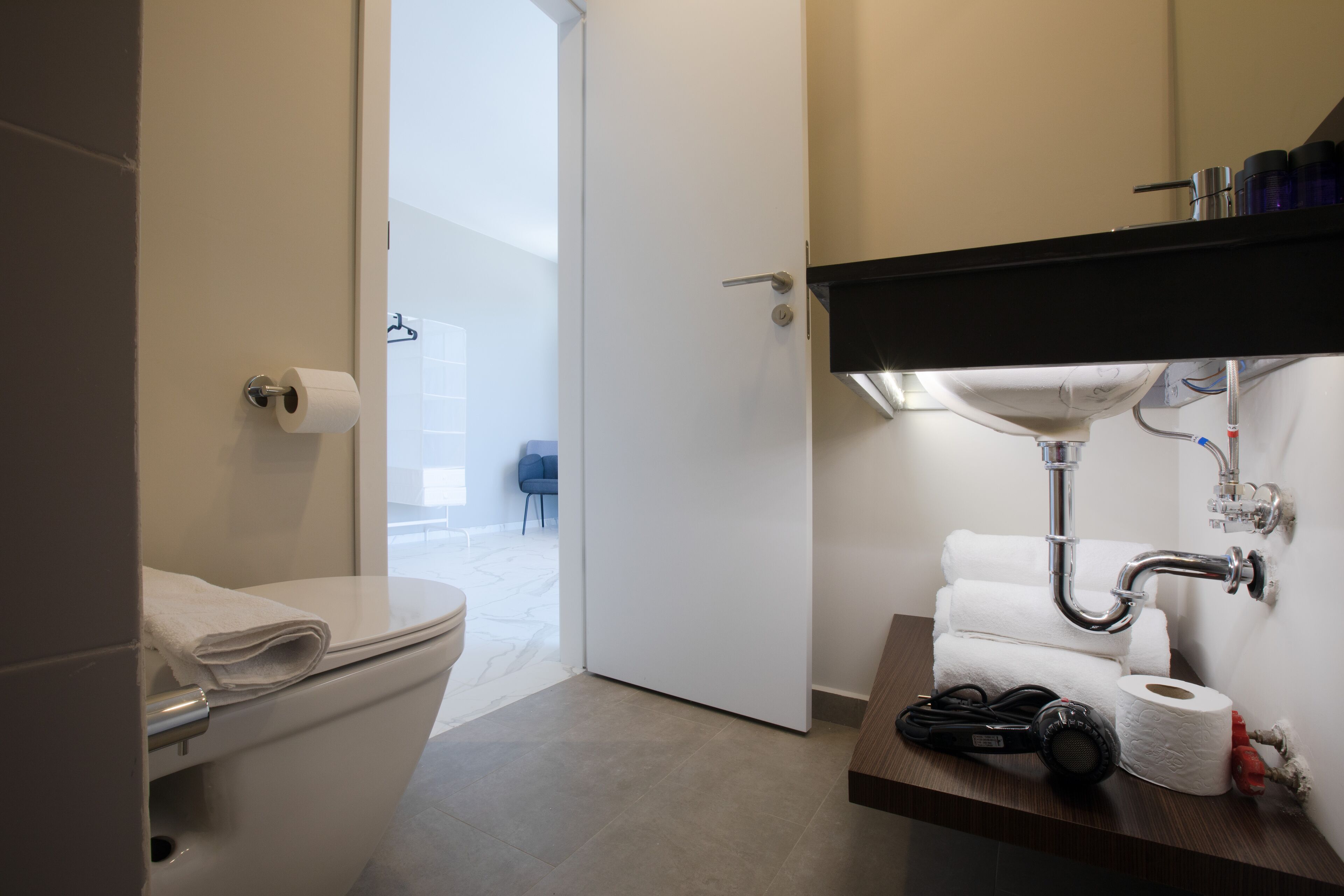 A modern bathroom with a toilet, a sink with a towel rack, and a visible door leading to another room.