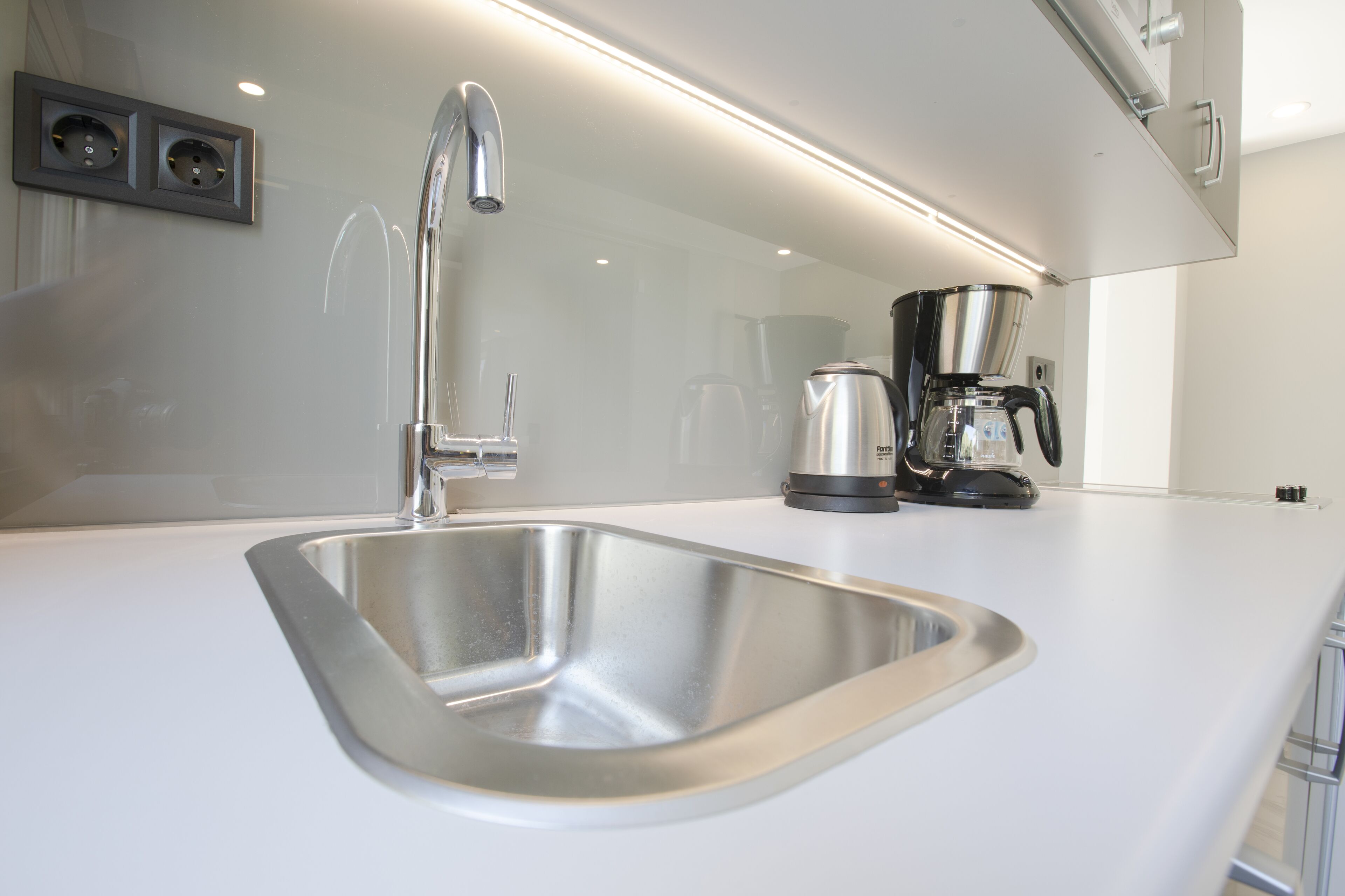 A modern kitchen with a stainless steel sink, a coffee maker, and a wall-mounted electrical outlet.