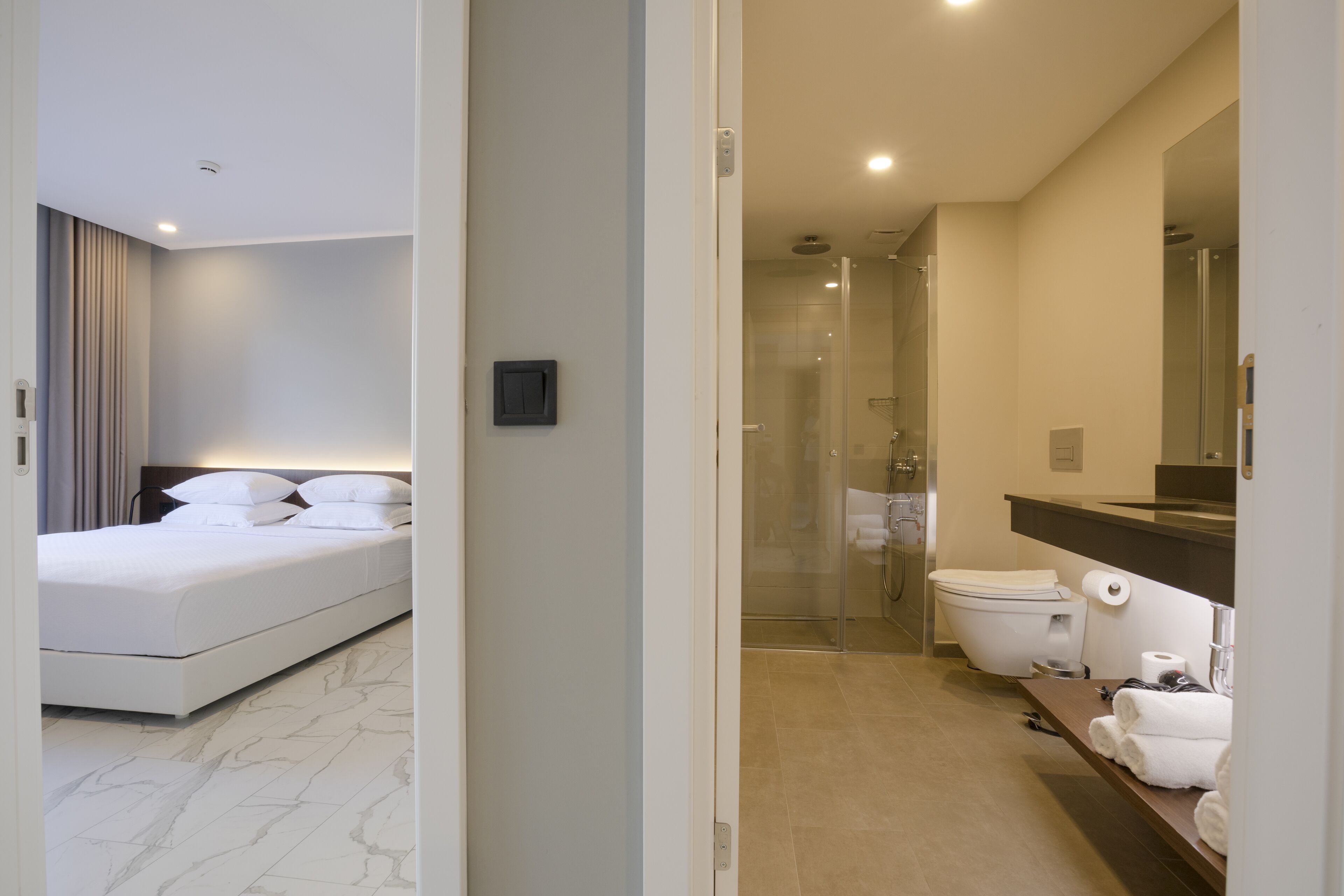 Une chambre d’hôtel moderne avec un lit bien fait, une salle de bain équipée d’une douche, de toilettes et d’un lavabo.