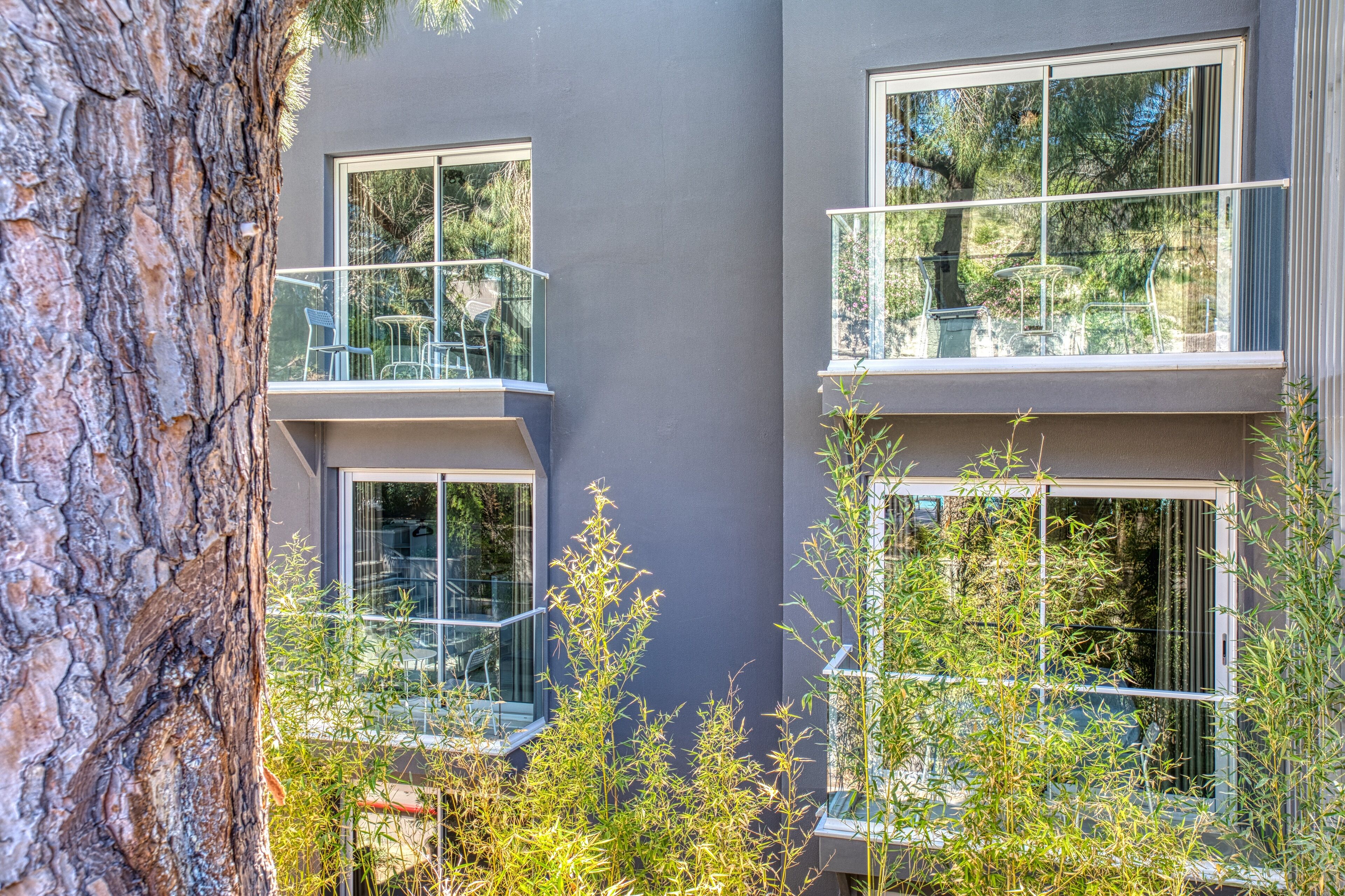 A modern building with multiple balconies, large windows, and surrounding greenery.