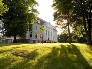 A large, historic building with a symmetrical facade, surrounded by a well-maintained lawn and mature trees. - The Gardener's House - Zinzow Castle (Boldekow)
