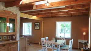 A rustic kitchen with wooden beams, a dining area with white chairs, and a large window providing natural light. - The Gardener's House - Zinzow Castle (Boldekow)