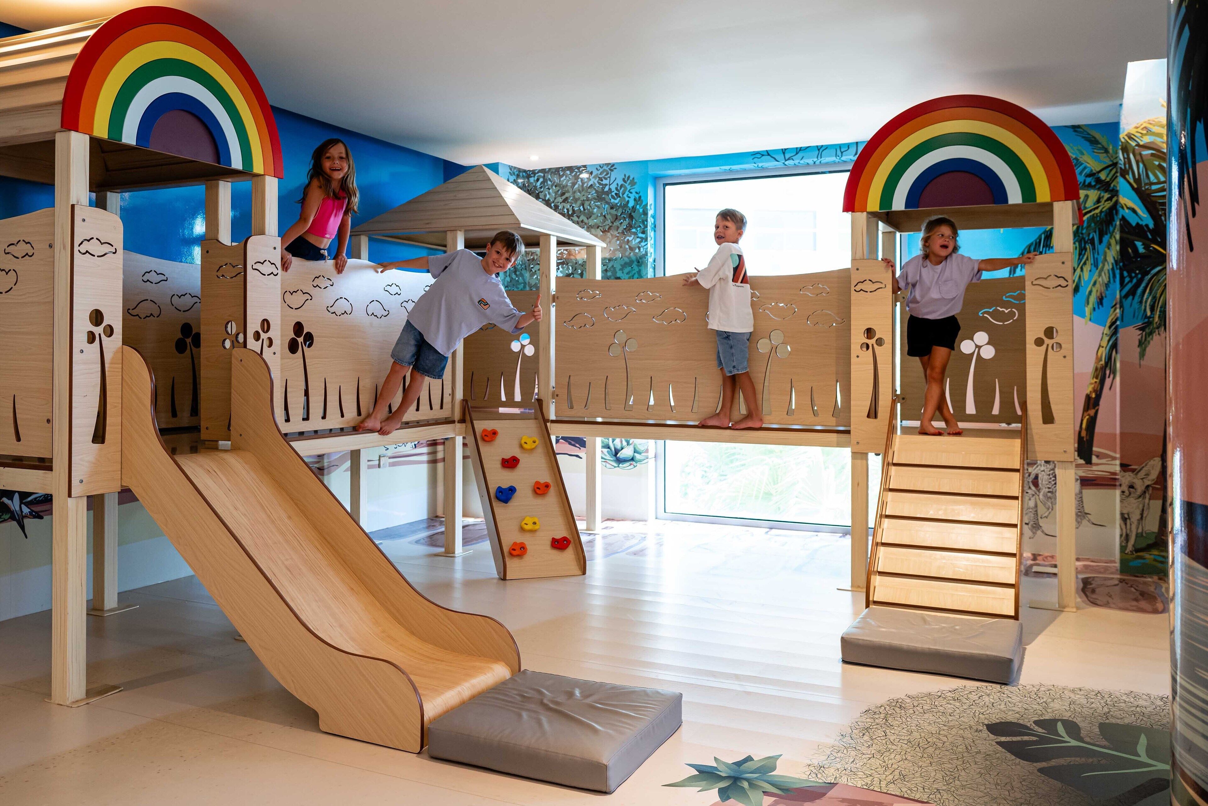 A children's play area with a slide, climbing wall, and a playhouse with a rainbow roof.