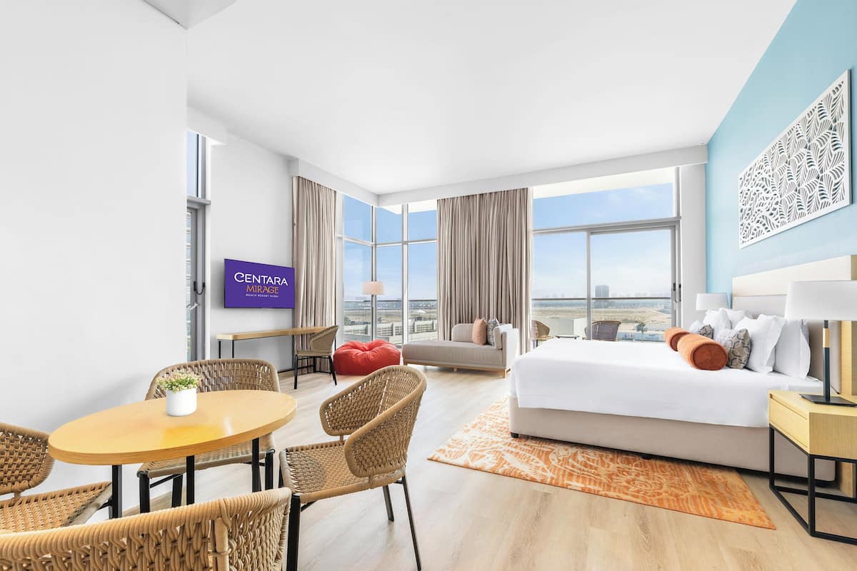 A hotel room with a bed, a desk, a chair, a table, a TV, and a large window with a city view.
