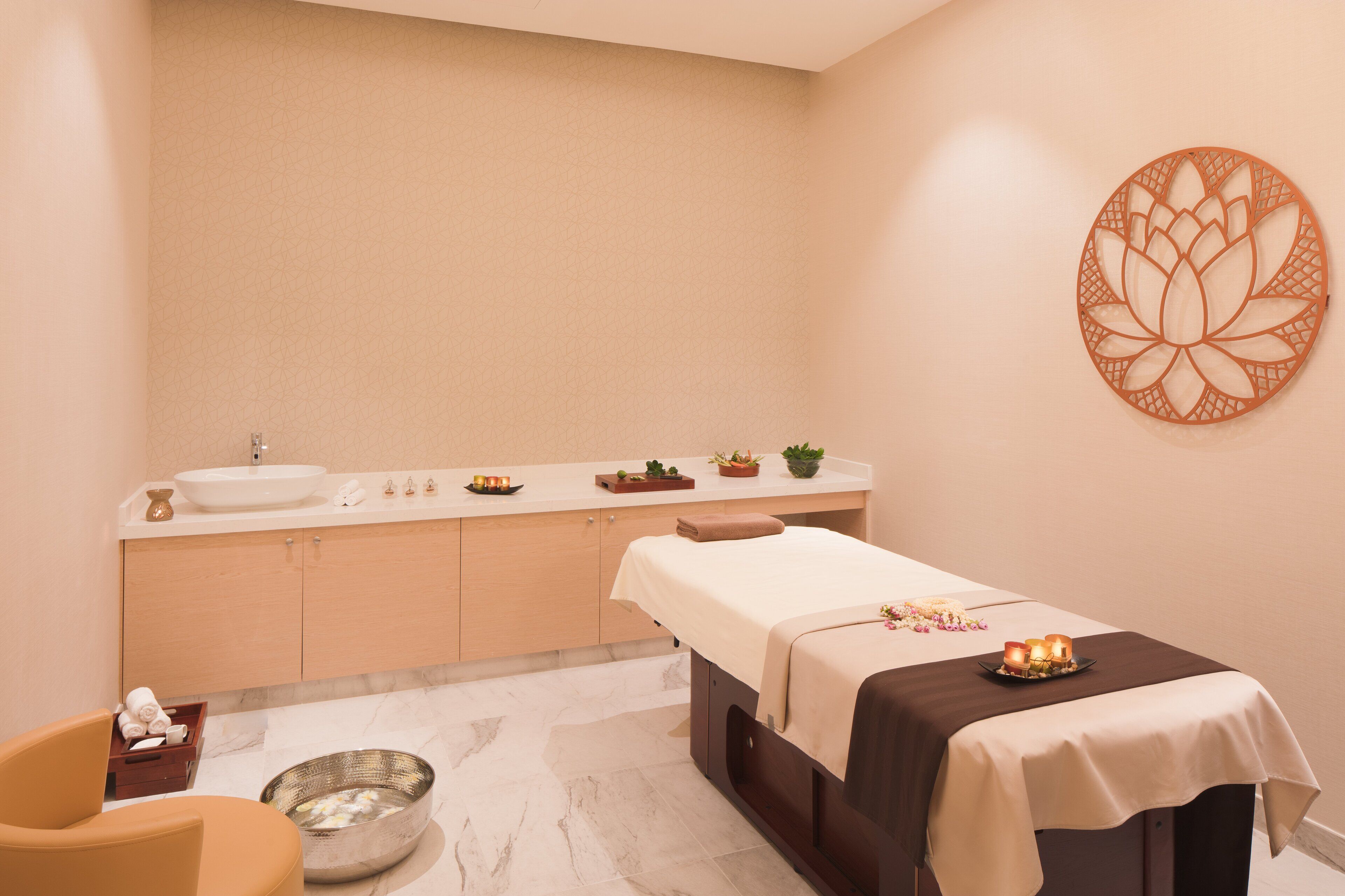 A spa room with a massage table, a sink, a mirror, and a decorative wall piece.