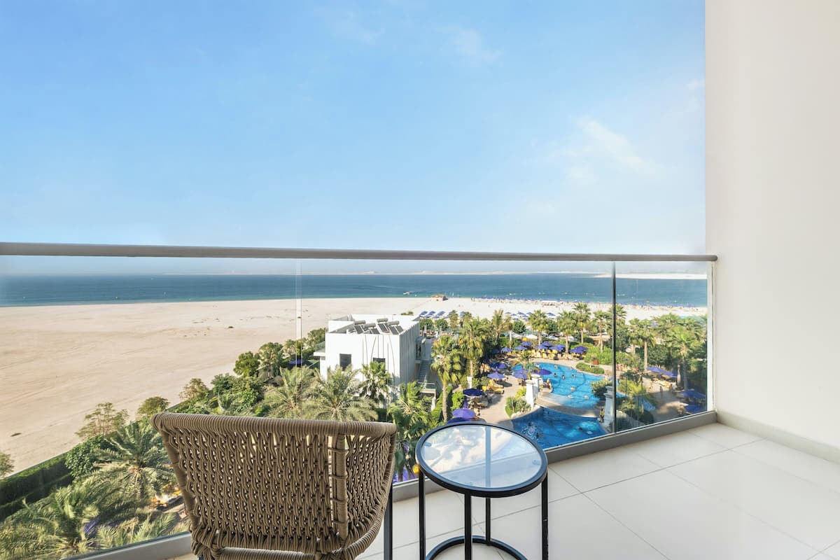 A balcony with a view of a beach, a pool, and a white building.
