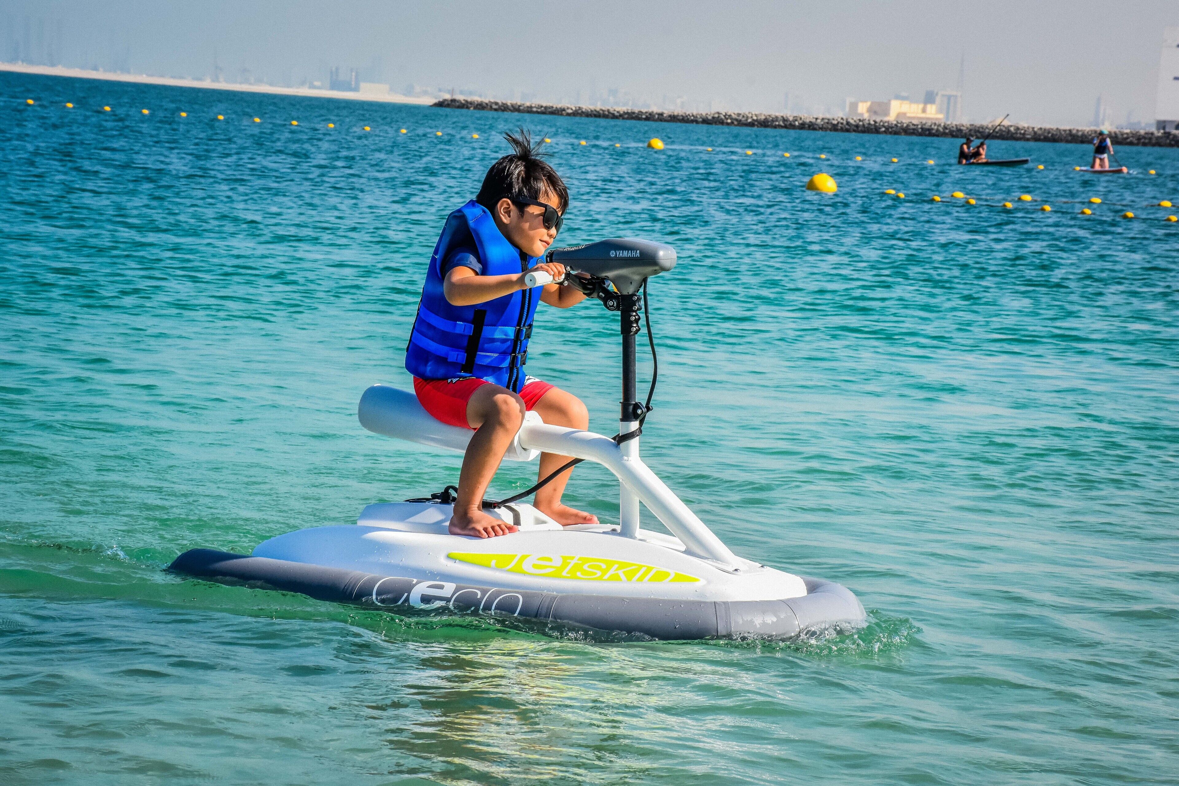 Una persona conduce un jet ski sobre el agua, con un horizonte urbano al fondo.