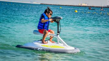 Una persona conduce un jet ski sobre el agua, con un horizonte urbano al fondo.