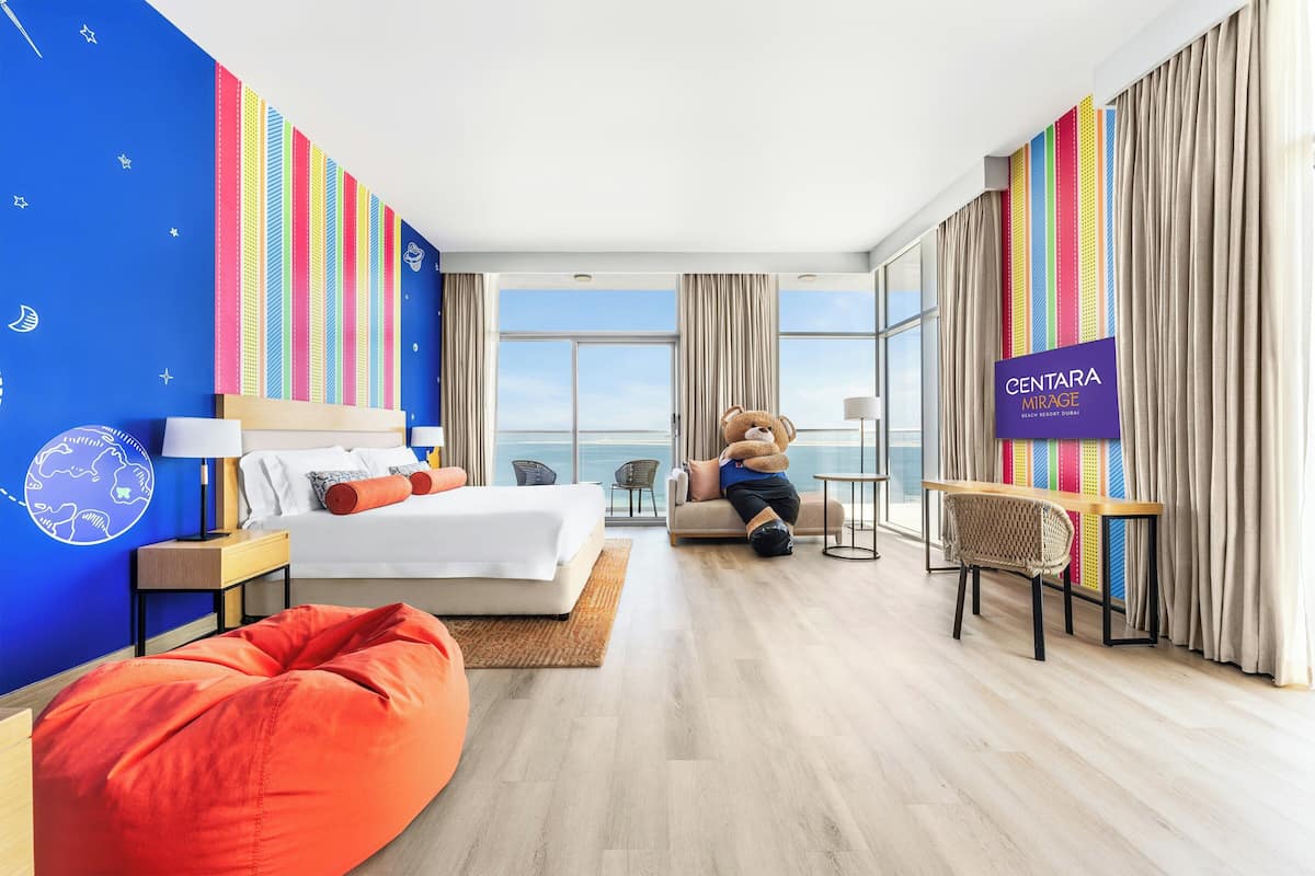 A modern hotel room with a large bed, a bean bag, a sofa, and a view of the city.
