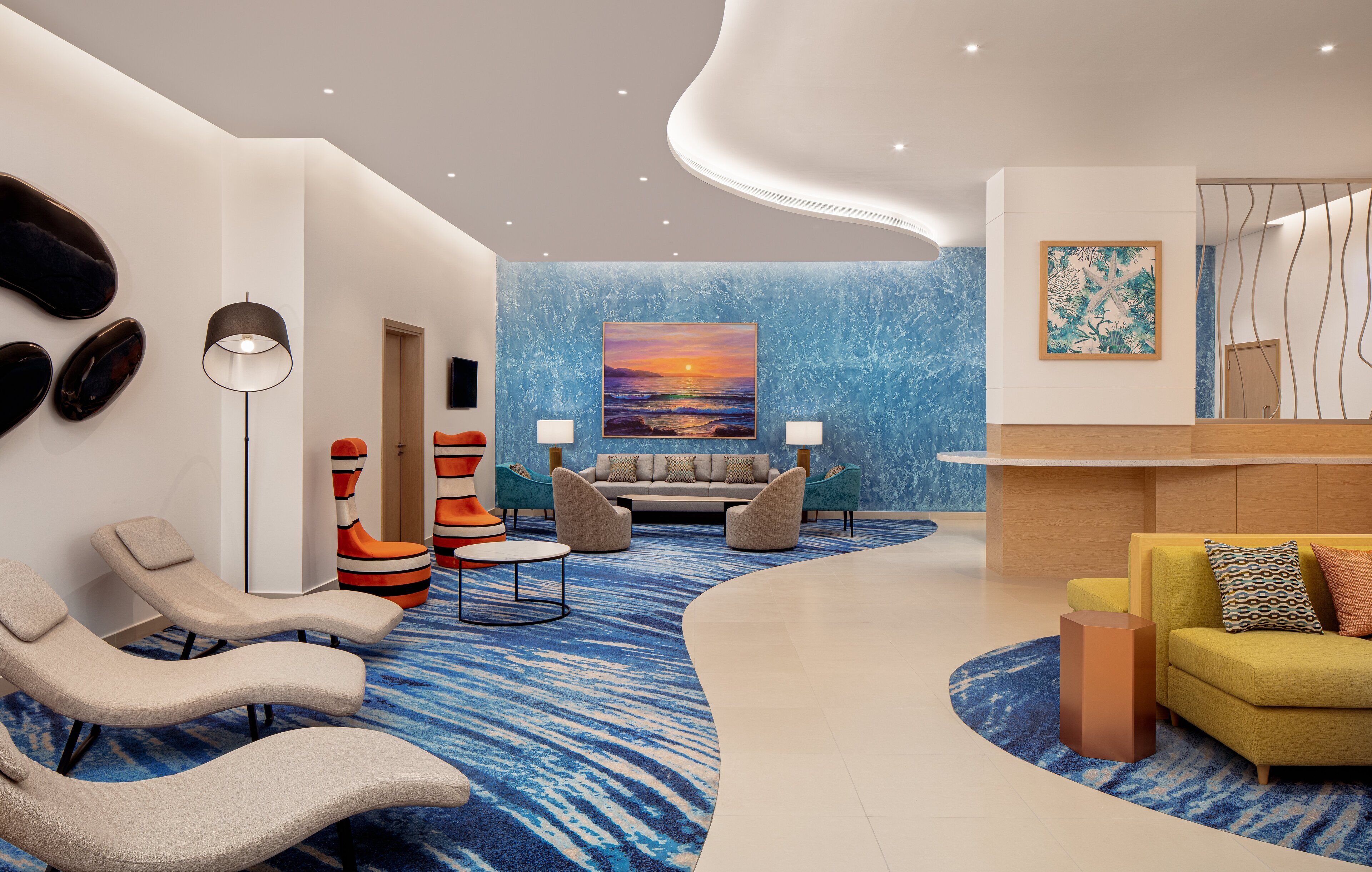 Un hall d'entrée moderne avec un tapis bleu, un comptoir d'accueil et des espaces aménagés pour s'asseoir.