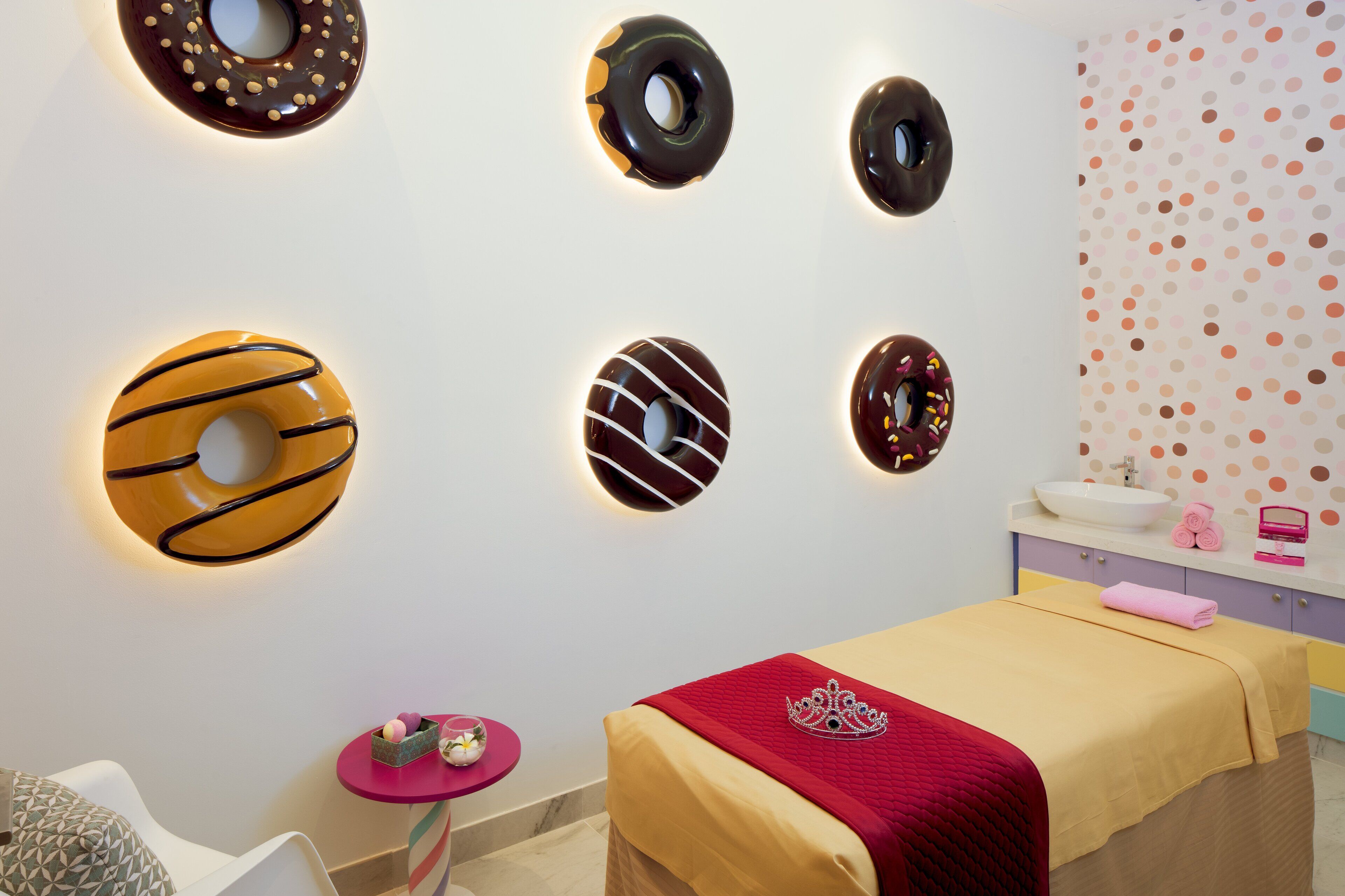 Ein Zimmer mit einem Bett, einem kleinen Tisch mit einer rosa Tischdecke und Wanddekorationen, die wie Donuts aussehen.