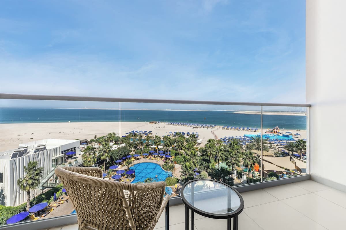 A balcony with a view of a beach, lounge chairs, and a pool.