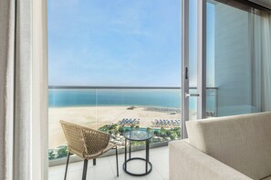 A balcony with a view of the beach, a wicker chair, a small round table, and a sofa.
