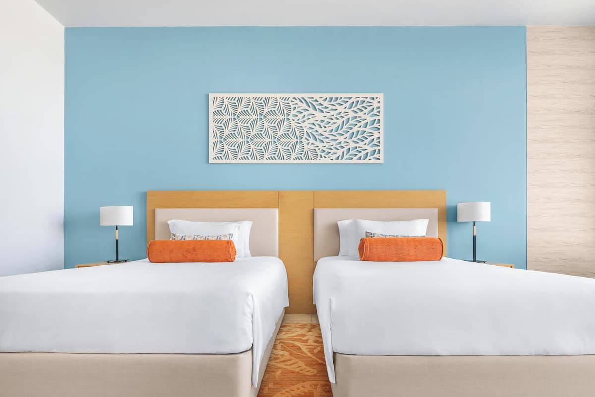 A hotel room with two beds, a blue accent wall, a decorative wall piece, and a wooden headboard.