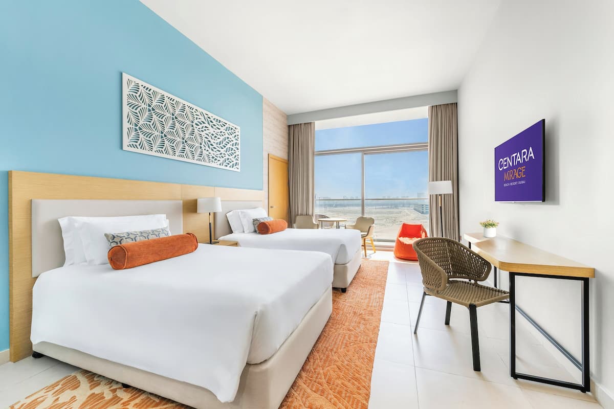 A hotel room with two beds, a desk, a chair, a view of the city, and a decorative wall piece.