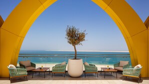 A balcony with a view of the beach, featuring a large planter with a tree, green wicker chairs, and a wooden table. - Centara Mirage Beach Resort Dubai (Dubai)