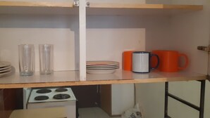 A kitchen counter with a stove, two glass tumblers, a stack of plates, a mug, and a small cabinet. - Tasumuka Savaal (Johannesburg)