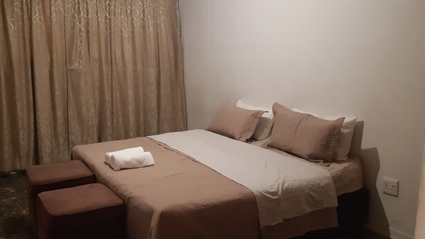 A bedroom with a bed, pillows, a blanket, and a bench. - Tasumuka Savaal (Johannesburg)