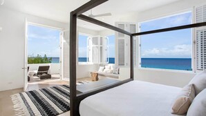 Ein Schlafzimmer mit einem großen Bett, einem Balkon mit Meerblick und einer Sitzecke mit Blick auf den Ozean.