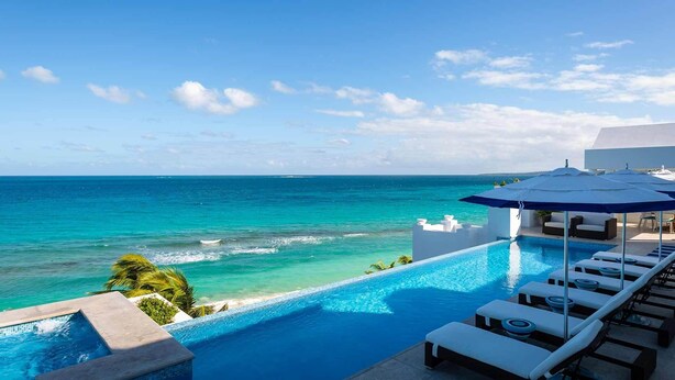 Ein Infinity-Pool mit Blick auf das Meer und den Strand, Liegestühle und Sonnenschirme.
