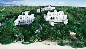 Eine weiße Villa mit Pool, umgeben von üppiger Vegetation und einem Strand.