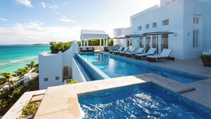 A pool area with lounge chairs and a view of the ocean. - Sand Villa – Greek-Inspired Elegance on the Shores of Long Bay, Anguilla (Long Bay Village)