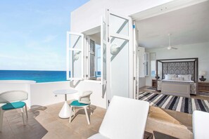 Un balcon avec vue sur l’océan, un lit avec une tête de lit à motifs et une petite table avec des chaises.