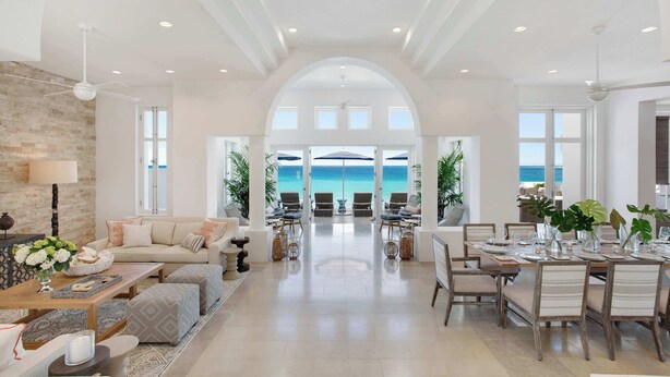 A spacious living area with a view of the ocean, a dining area with a table set for six, and a cozy seating area with a sofa and cushions. - Sand Villa – Greek-Inspired Elegance on the Shores of Long Bay, Anguilla (Long Bay Village)