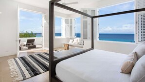 A bedroom with a large bed, a view of the ocean, and a balcony with outdoor seating. - Sand Villa – Greek-Inspired Elegance on the Shores of Long Bay, Anguilla (Long Bay Village)