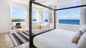 Une chambre dotée d’un grand lit, offrant une vue sur l’océan et comprenant un balcon avec des sièges d’extérieur.